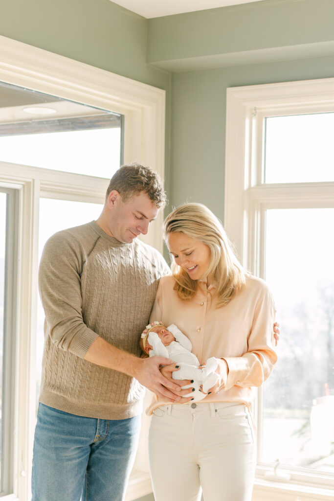 young couple hold newborn baby girl pose for photographer in dayton area home with family dog 