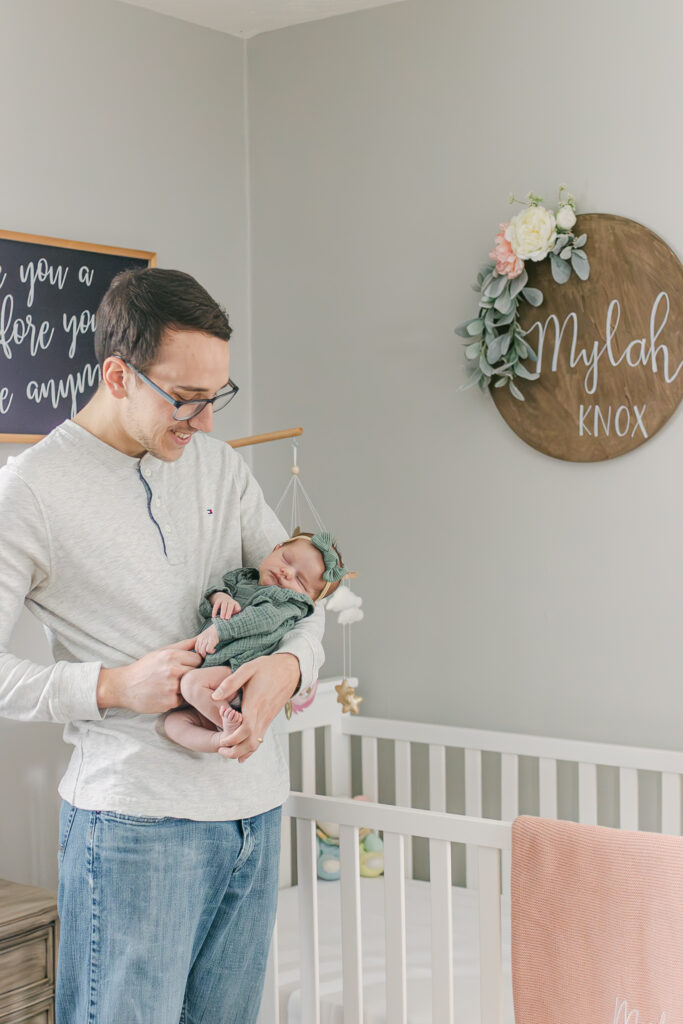 father holds newborn daughter in nursery as dayton ohio photographer takes pictures