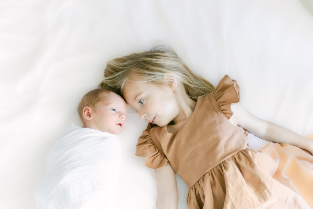 young girl cuddles newborn baby brother 