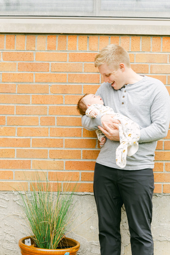 father holds new infant son in front of dayton ohio area home as professional photographer takes picture