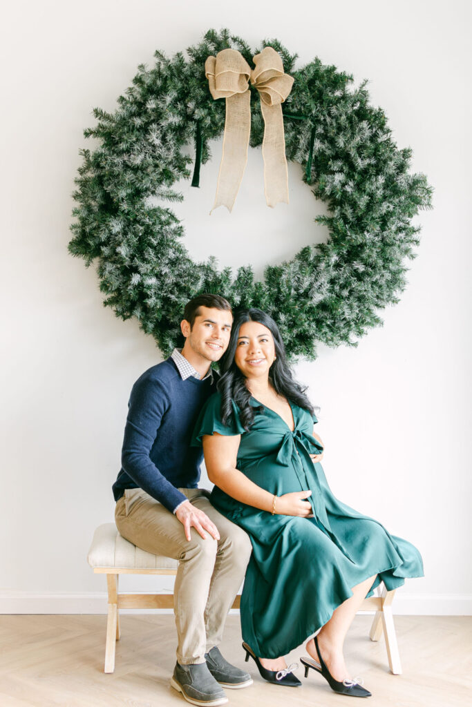 Expectant mother and father posing together in front of a holiday wreath during a studio maternity photography session near Mariemont, Ohio.