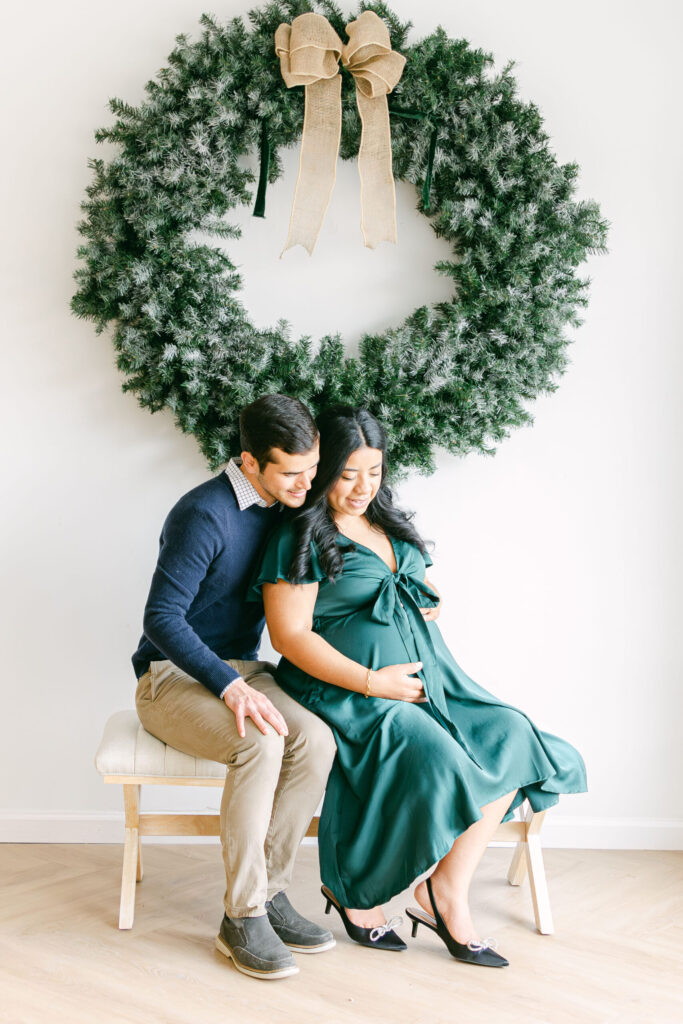 Expectant mother and father posing together in front of a holiday wreath during a studio maternity photography session near Mariemont, Ohio.