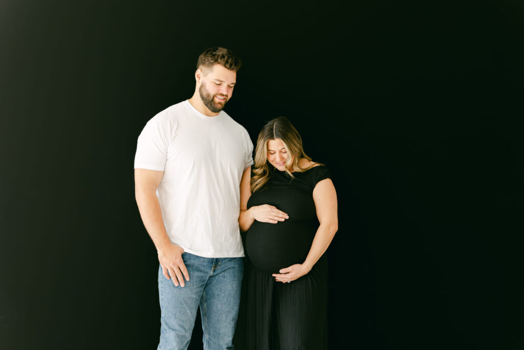 mom and dad smiling down at newborn baby bump for studio maternity session in cincinnati