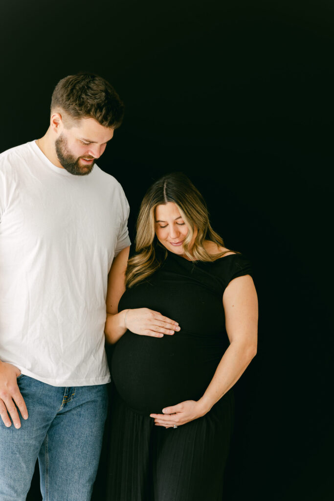 mom and dad smiling down at newborn baby bump for cincinnati studio matenrity session